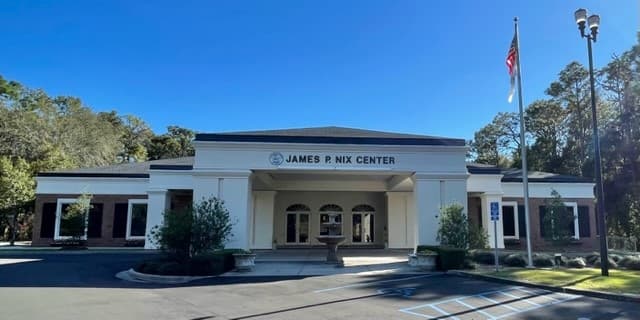 The James P. Nix Center: a white single-storey building with a columned entrance and its name over the door, with the American flag flying beside the car park.